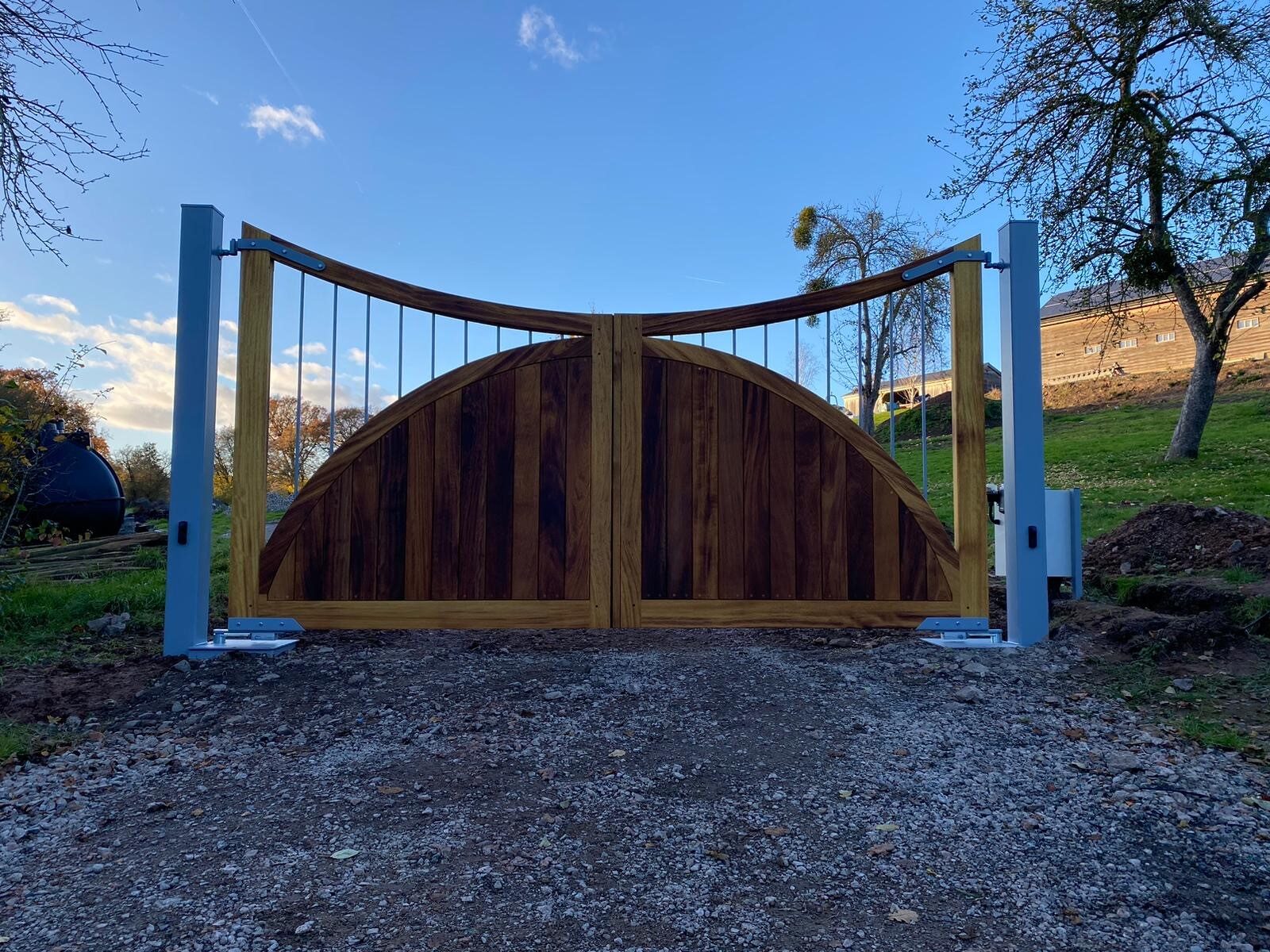 Hardwood driveway gates with a deep arched top hung on painted steel posts
