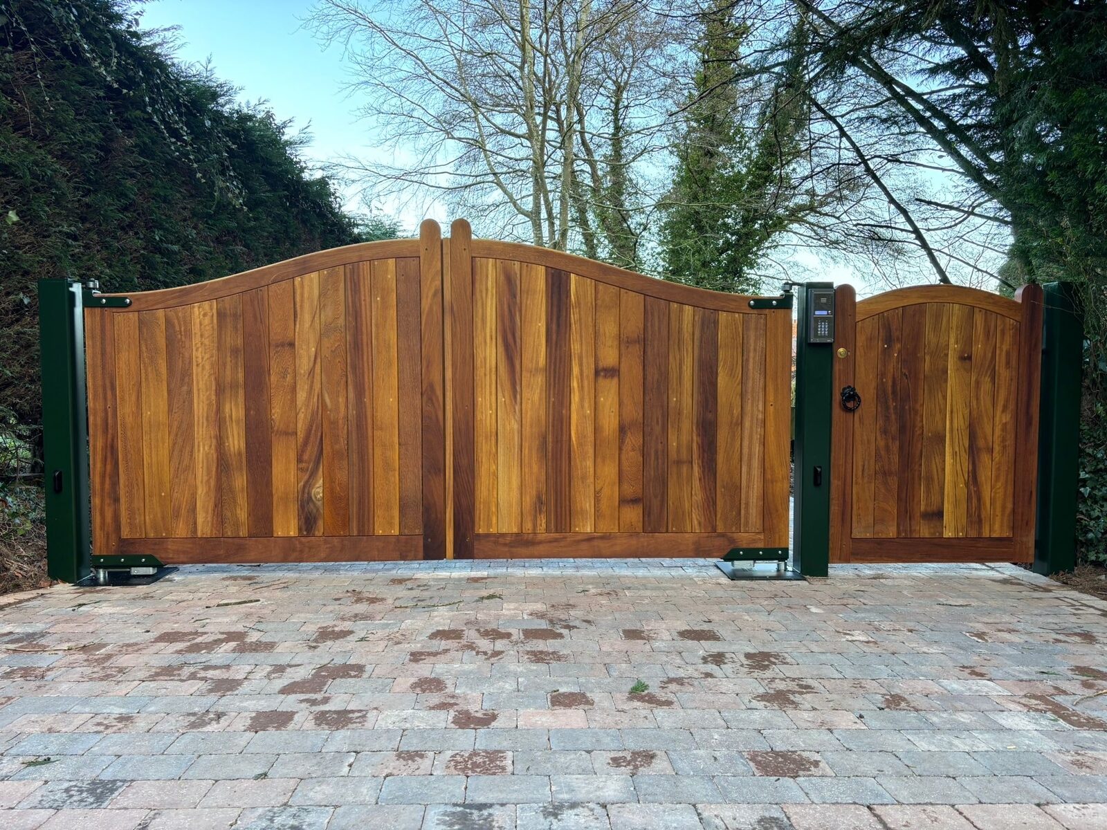 Hardwood driveway gates with curved top and matching pedestrian gate on a block paved drive