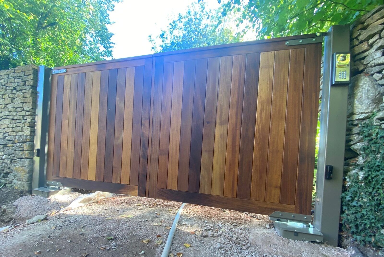 Tall hardwood sliding gate with vertical board infill on a Cotswold stone driveway