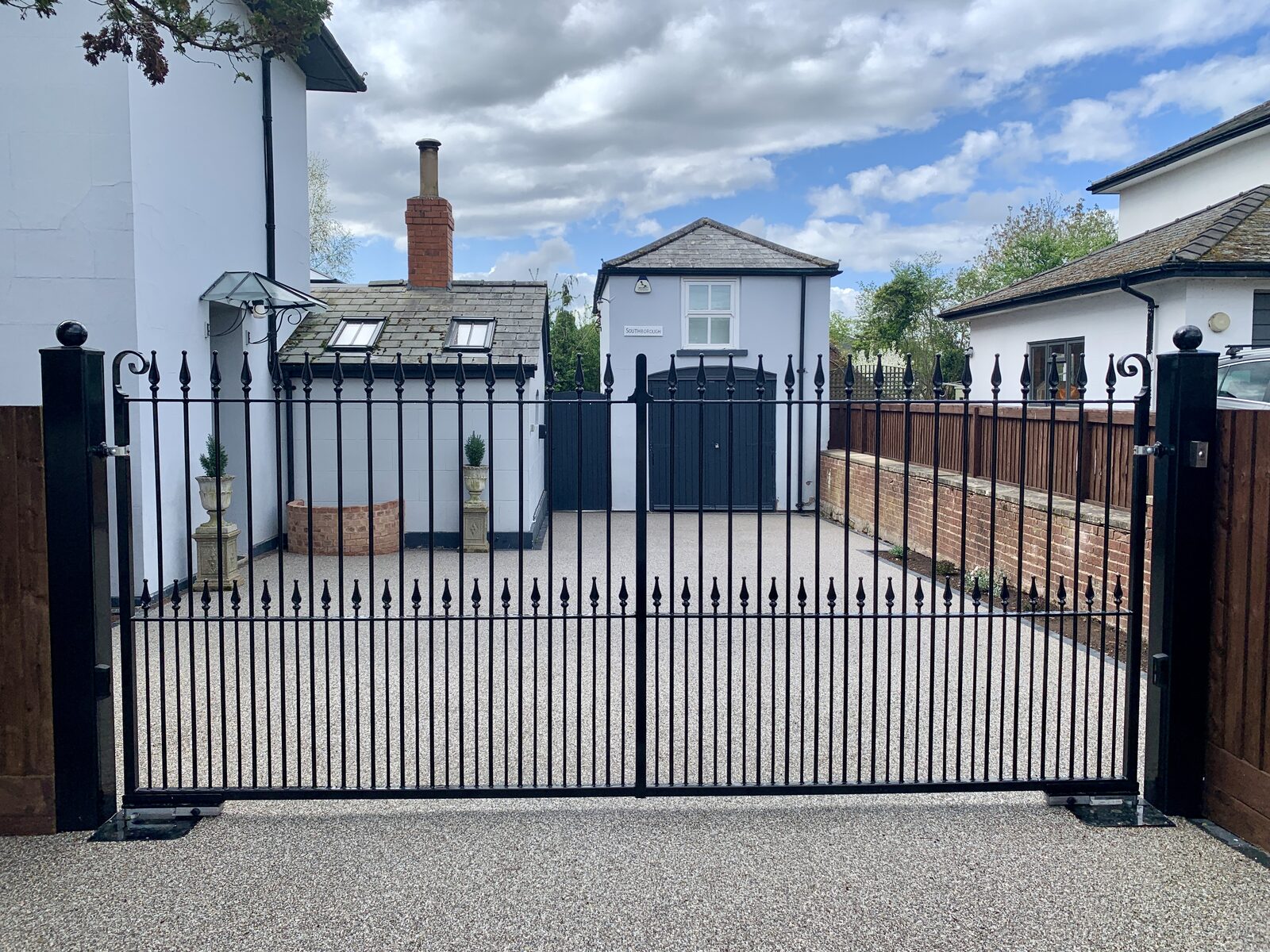 Black steel driveway gates with vertical railing infill at a white rendered house