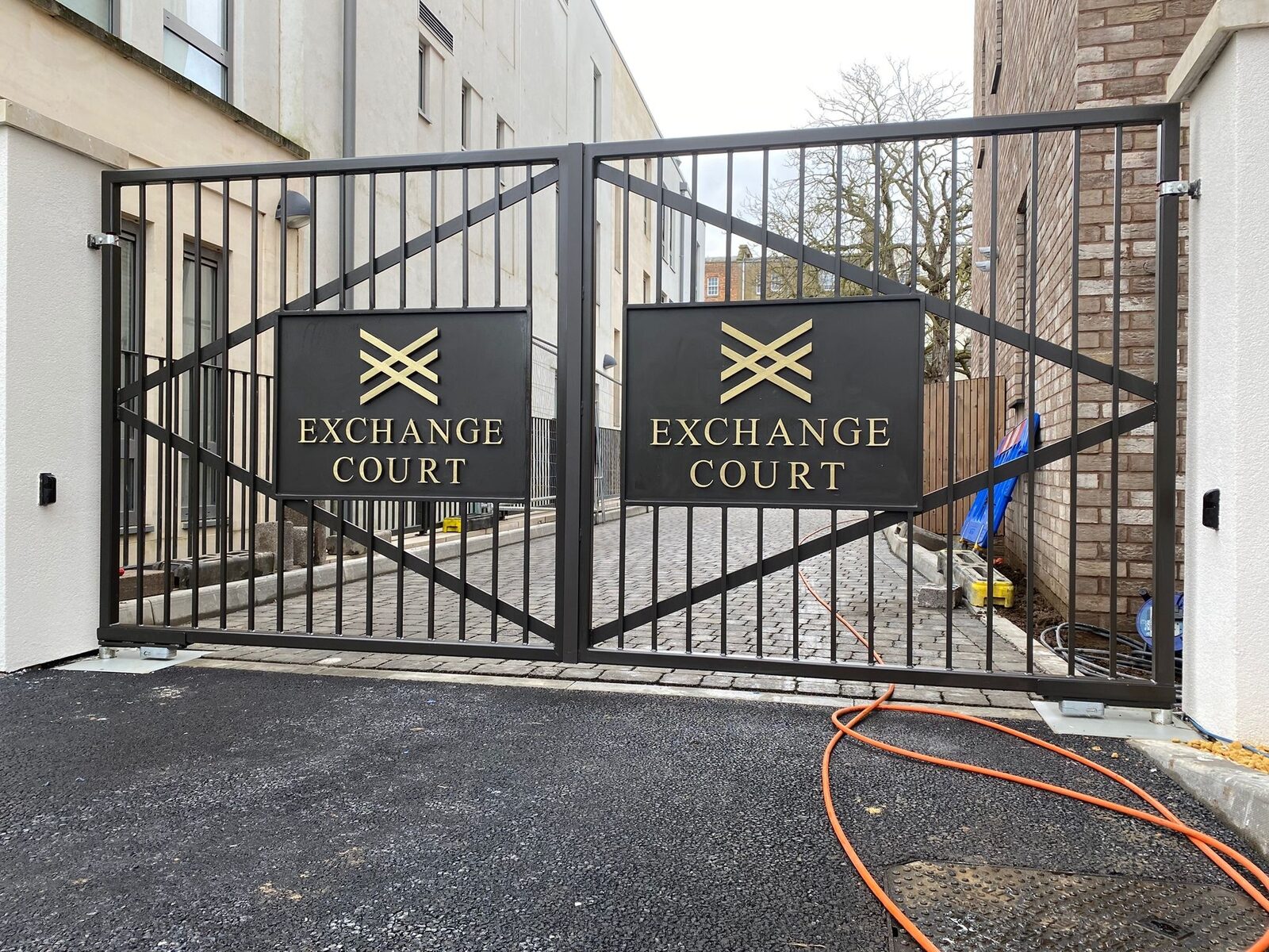 Black steel driveway gates with diagonal bracing and engraved name plaques
