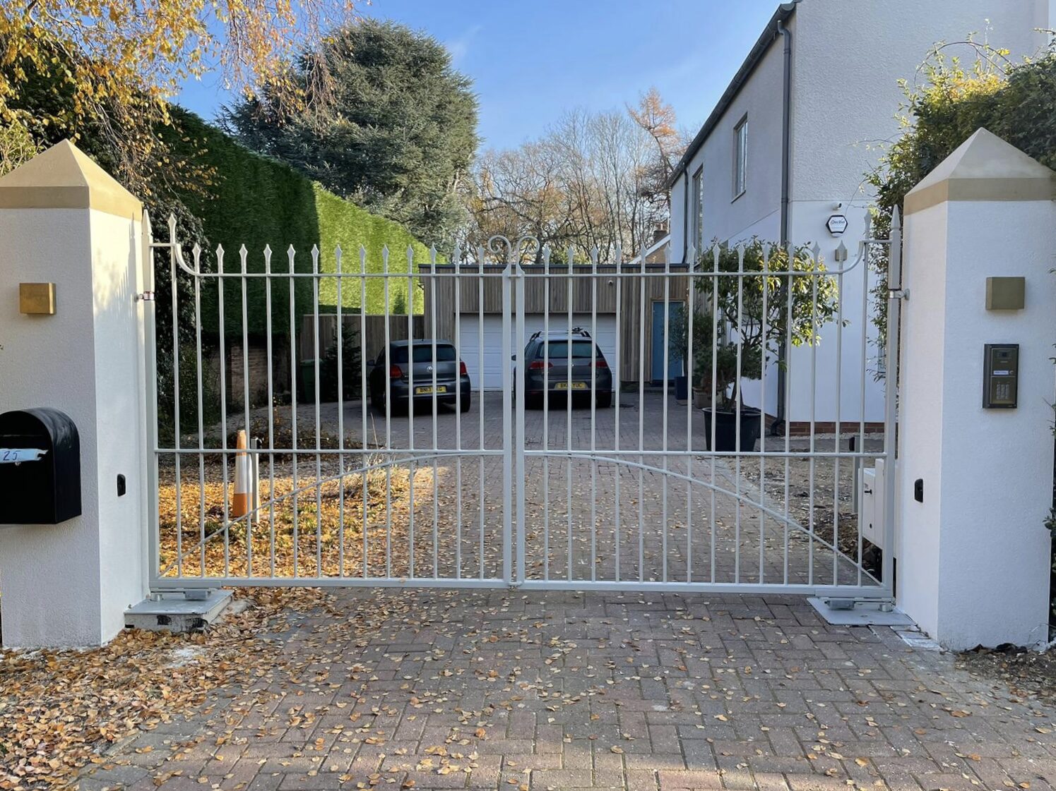 White painted steel driveway gates with arched top and spear railheads between rendered pillars