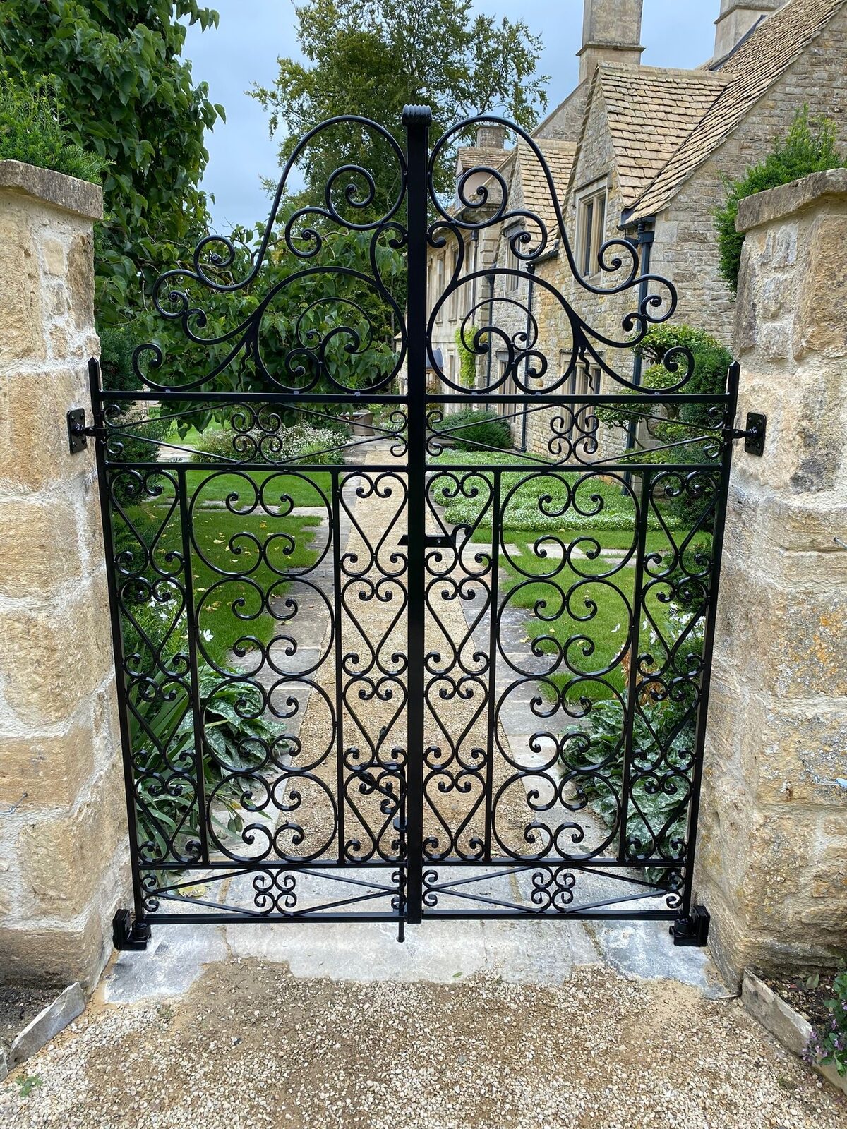 Ornate black wrought iron pedestrian gate with scrollwork set in a stone archway